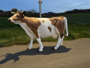 braun-weisse kuh als gartenfigur in einer weiten seitenansicht